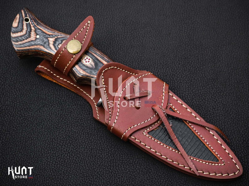 May include: A brown leather sheath with a black and brown wooden handle knife. The sheath has a decorative stitching pattern and a strap with a knot.