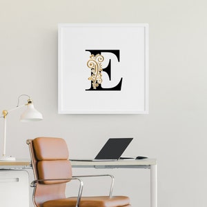May include: A white framed print with a black letter E and a gold floral design.