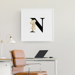May include: A white framed print with a black letter N and a gold floral design.