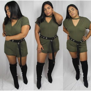 Op de afbeelding: Olijfgroene romper met een V-hals en korte mouwen. De romper is in de taille getailleerd met een zwarte riem met zilveren ogen. De outfit wordt gecombineerd met zwarte over-the-knee laarzen.