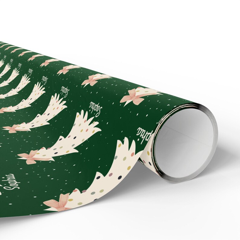 May include: Green wrapping paper with a repeating pattern of white Christmas trees with pink bows and gold polka dots. The trees have the name "Sophia" written on them.