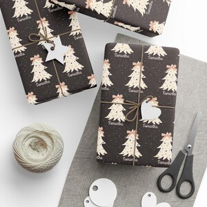 May include: A black and white wrapping paper with a repeating pattern of stylized Christmas trees with gold dots and pink bows. The name "Samantha" is repeated throughout the pattern.