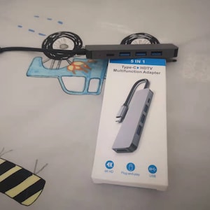 May include: A grey 5-in-1 Type-C HDTV Multifunction Adapter with a white cable and connectors. The adapter has a 4K HD output, a USB port, and a plug-and-play feature.