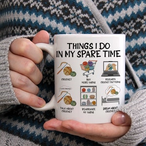 May include: White ceramic mug with the text "Things I do in my spare time" and illustrations of yarn, crochet hooks, and shopping carts. The text below the illustrations includes "crochet", "buy more yarns", "research crochet patterns", "talk about crochet", "rearrange my yarns", and "dream about crochet".