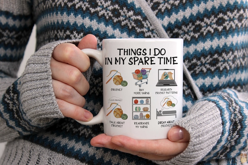 May include: White ceramic mug with the text "Things I do in my spare time" and illustrations of yarn, crochet hooks, and shopping carts. The text below the illustrations includes "crochet", "buy more yarns", "research crochet patterns", "talk about crochet", "rearrange my yarns", and "dream about crochet".