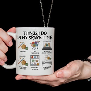 May include: White ceramic mug with a black outline and the text "Things I do in my spare time" with illustrations of yarn, crochet hooks, and a laptop. The text below the illustrations includes "crochet", "buy more yarns", "research crochet patterns", "talk about crochet", "rearrange my yarns", and "dream about crochet".