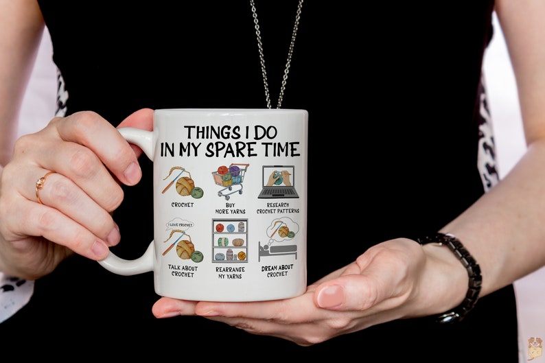 May include: White ceramic mug with a black outline and the text "Things I do in my spare time" with illustrations of yarn, crochet hooks, and a laptop. The text below the illustrations includes "crochet", "buy more yarns", "research crochet patterns", "talk about crochet", "rearrange my yarns", and "dream about crochet".