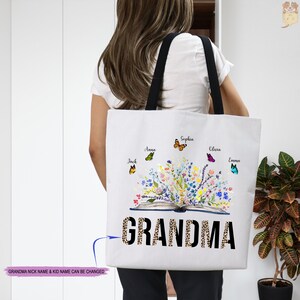 May include: White tote bag with a black handle. The bag features a colorful illustration of an open book with flowers and butterflies. The text "GRANDMA" is printed in black with a leopard print pattern.