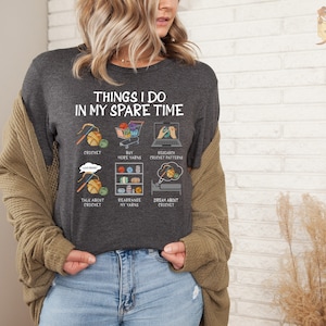 May include: A dark gray t-shirt with the text "Things I do in my spare time" and illustrations of crocheting, buying yarn, researching crochet patterns, talking about crochet, rearranging yarn, and dreaming about crochet.