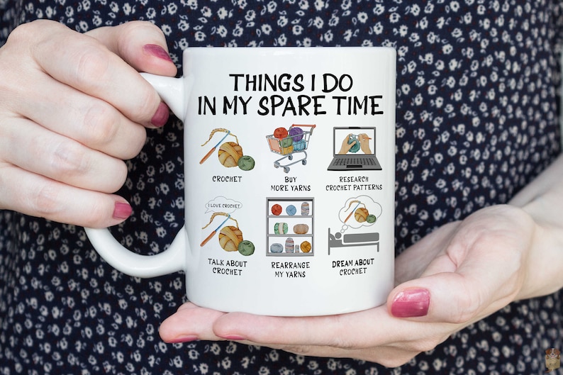 May include: White ceramic mug with a black and white illustration of things a crocheter does in their spare time. The text reads "Things I do in my spare time". The illustrations include crocheting, buying more yarn, researching crochet patterns, talking about crochet, rearranging yarn, and dreaming about crochet.