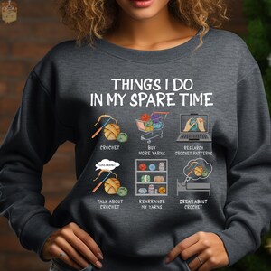 May include: A gray sweatshirt with the text "Things I do in my spare time" and illustrations of crocheting, buying yarn, researching crochet patterns, talking about crochet, rearranging yarn, and dreaming about crochet.