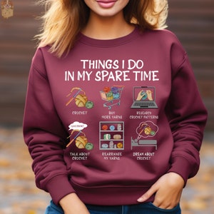 May include: A maroon sweatshirt with the text "Things I do in my spare time" and illustrations of crocheting, buying yarn, researching crochet patterns, talking about crochet, rearranging yarn, and dreaming about crochet.