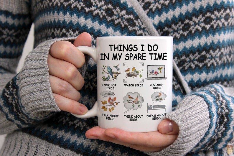 May include: White ceramic coffee mug with a black design that says "Things I do in my spare time" and lists activities related to birds. The activities include looking for birds, watching birds, researching birds, talking about birds, thinking about birds, and dreaming about birds.