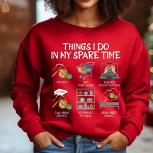 May include: Red sweatshirt with the text "Things I do in my spare time" and illustrations of crocheting, buying yarn, researching crochet patterns, talking about crochet, rearranging yarn, and dreaming about crochet.