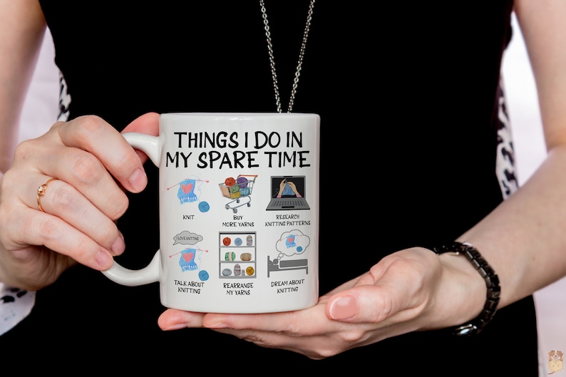 May include: White ceramic mug with a black outline and the text "Things I do in my spare time". The mug has illustrations of knitting needles, yarn, a shopping cart, a laptop, and a bed.