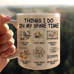May include: White ceramic mug with a black and white design. The mug features the text "Things I do in my spare time" and illustrations of birds. The text below the illustrations includes phrases like "Look for birds", "Watch birds", "Research birds", "Talk about birds", "Think about birds", and "Dream about birds".