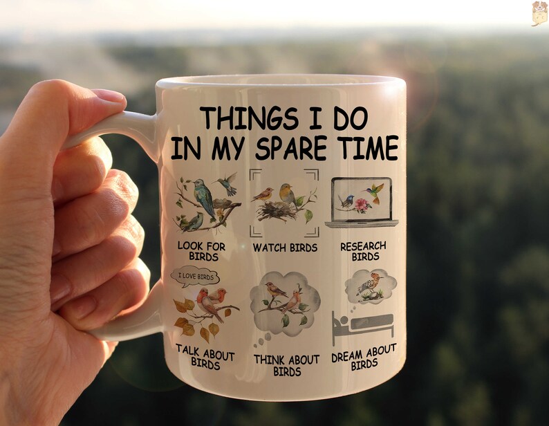 May include: White ceramic mug with a black and white design. The mug features the text "Things I do in my spare time" and illustrations of birds. The text below the illustrations includes phrases like "Look for birds", "Watch birds", "Research birds", "Talk about birds", "Think about birds", and "Dream about birds".