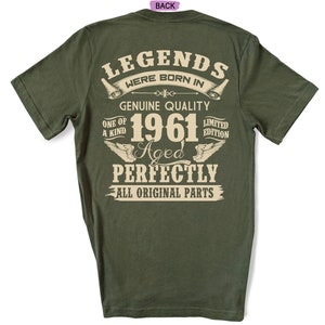 Op de afbeelding: Een groen T-shirt met de tekst "Legends were born in 1961 Aged Perfectly All Original Parts" in beige. De tekst wordt omringd door decoratieve elementen.