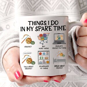 May include: White ceramic mug with a black outline and the text "Things I do in my spare time". The mug features illustrations of yarn, crochet hooks, and a shopping cart. The text "Crochet", "Buy more yarns", "Research crochet patterns", "Talk about crochet", "Rearrange my yarns", and "Dream about crochet" are written below the illustrations.