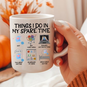 May include: White ceramic mug with a black outline of a person knitting and the text "Things I do in my spare time". The mug has illustrations of knitting related activities, including knitting, buying yarn, researching knitting patterns, talking about knitting, rearranging yarn, and dreaming about knitting.