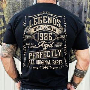 May include: Black t-shirt with a vintage design. The design includes the text "LEGENDS WERE BORN IN 1986" in a decorative font, along with the phrases "Genuine Quality", "One of a Kind", "Aged Perfectly", and "All Original Parts".