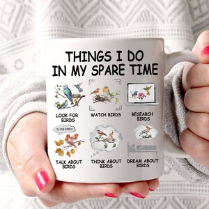 May include: White ceramic mug with a black and gray design. The mug features the text "Things I do in my spare time" and illustrations of birds. The text below the illustrations includes "Look for birds", "Watch birds", "Research birds", "Talk about birds", "Think about birds", and "Dream about birds".