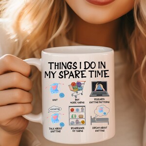 May include: White ceramic mug with the text "Things I do in my spare time" and illustrations of knitting, yarn, and a laptop. The illustrations are accompanied by text describing activities related to knitting, such as "Knit", "Buy more yarns", "Research knitting patterns", "Talk about knitting", "Rearrange my yarns", and "Dream about knitting".