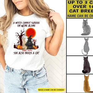 Op de afbeelding: Wit T-shirt met een Halloween-thema ontwerp met een heks, twee katten en de tekst "Een heks kan niet alleen van wijn leven. Ze heeft ook een kat nodig." De namen "Cooper" en "Jessica" staan onder de katten.