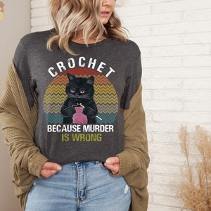 May include: A dark gray t-shirt with a vintage-style graphic of a black cat crocheting with the text "Crochet because murder is wrong".