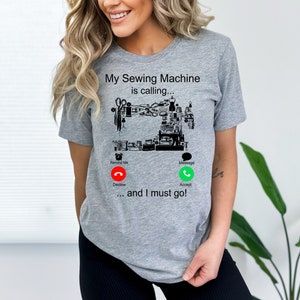 May include: A gray t-shirt with a black illustration of a sewing machine with the text "My Sewing Machine is calling... and I must go!"  The illustration includes a phone icon with a red decline button and a green accept button.