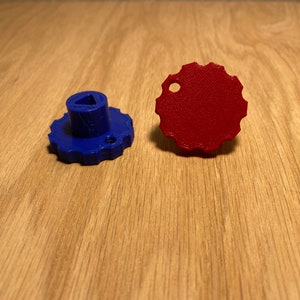 May include: Two plastic knobs, one blue and one red. The blue knob has a triangular hole in the top and a raised, textured surface. The red knob is round and has a smooth surface.