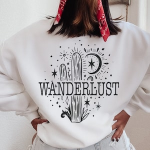 May include: White sweatshirt with a black and white graphic of a cactus, a crescent moon, stars, and the word "WANDERLUST".