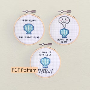 Op de afbeelding: Drie borduurpatronen in de vorm van hoepels met woordspelingen over schelpen. De eerste hoepel zegt "Keep Clam and Make Puns". De tweede hoepel zegt "Happy as a Clam". De derde hoepel zegt "I find it difficult to open up to people".