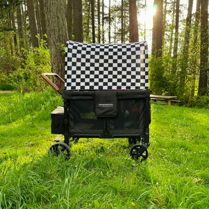May include: A black utility wagon with a checkered canopy is positioned on a grassy area, surrounded by trees. The wagon has black wheels and a wooden handle. The canopy features a black and white checkerboard pattern. The text "WonderFold" is visible.