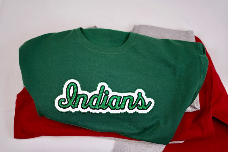 May include: A green sweatshirt with a white and green embroidered patch that says "Indians" on it.
