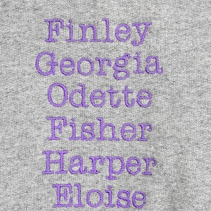 May include: A gray sweatshirt with purple embroidery that reads "Finley Georgia Odette Fisher Harper Eloise".