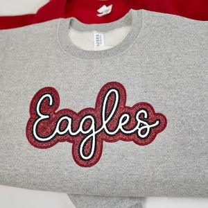 May include: Gray sweatshirt with a red glitter "Eagles" design.
