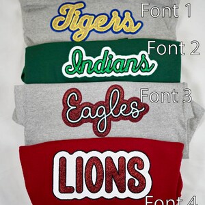 May include: Four sweatshirts with different colored fabric and different glittery iron-on letters. The letters spell out "Tigers", "Indians", "Eagles", and "Lions". Each sweatshirt has a number next to it, indicating the font style of the letters. Font 1, Font 2, Font 3, and Font 4.