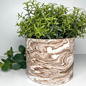 May include: A white ceramic planter with brown marbling, featuring a green leafy plant.
