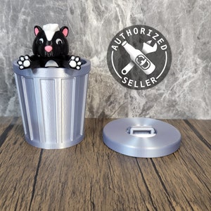 May include: A silver trash can with a black and white skunk figurine inside. The trash can has a lid with a silver handle. The trash can is sitting on a wooden surface. The image also includes a black and white sticker with the text "AUTHORIZED SELLER" and a wrench and bottle icon.