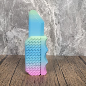 May include: A colourful, 3D printed, plastic knife with a textured, scale-like pattern. The knife is a gradient of pink, blue and green.