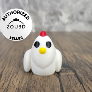 May include: White 3D printed chicken figurine with black eyes, a yellow beak, and a red comb. The figurine is sitting on a wooden surface.
