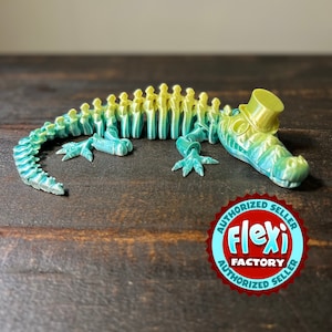 May include: A green and yellow 3D printed alligator skeleton wearing a top hat. The alligator is lying on a wooden surface. The image includes a red and white sticker with the text "Authorized Seller Flexi Factory Authorized Seller".