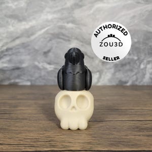 May include: A black 3D printed parrot perched atop a white 3D printed skull. The skull has two eye sockets and a prominent nose. The parrot has a rounded head and a beak. The image includes a circular sticker with the text "AUTHORIZED ZOU3D SELLER".