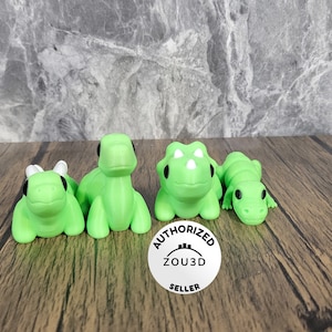 May include: Four green dinosaur figurines with black eyes. The dinosaurs are in various poses, including standing, sitting, and lying down. The figurines are on a wooden surface. The text "AUTHORIZED ZOU3D SELLER" is on a white circle sticker.