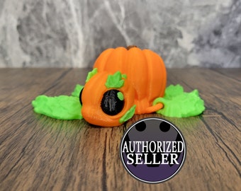 May include: A small orange pumpkin with green leaves and black eyes. The pumpkin is lying on a wooden surface.