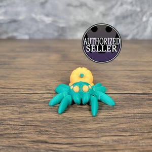 Peut inclure: Une figurine d'araignée imprimée en 3D de couleur turquoise et jaune. L'araignée a un corps rond et jaune avec une tache verte sur le dessus et trois paires de pattes turquoise.