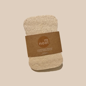 May include: A beige, rectangular, compostable sponge with a brown label that reads "m noel COMPOSTABLE SPONGE eco-friendly | all natural | plant-based"