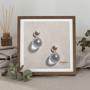 May include: A framed illustration of a pair of pearl earrings with gold accents. The earrings are depicted on a beige background with subtle shadows.