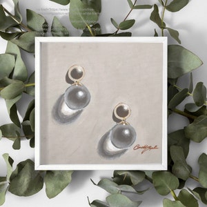 May include: A pair of gold and gray pearl earrings with a simple design. The earrings are displayed on a light brown background.